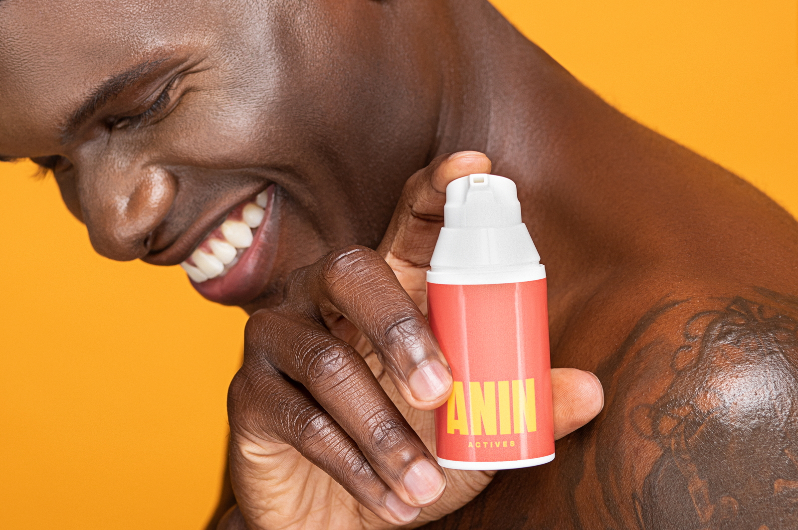 Male model with tatoo on his left sholder holding an ANIN Actives presctiption bottles. The ANIN Actives bottle has white dispenser and red label with a ANIN Actives logo in yellow.